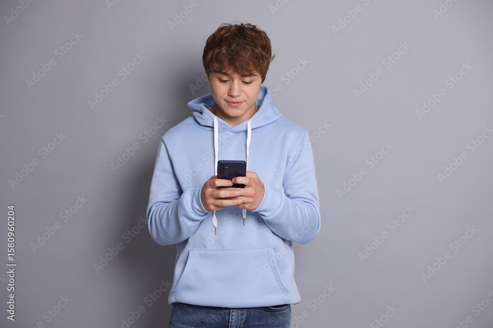 Teenage boy using smartphone on grey background Teenage boy using smartphone on grey background