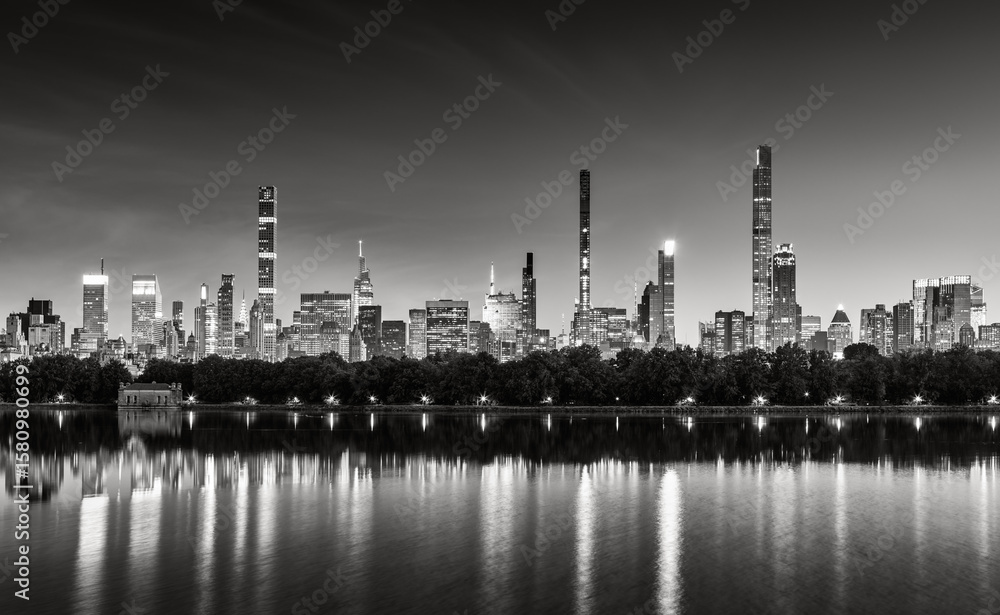 Naklejka premium New York City skyline at dusk with reflections of Billionaires Row supertall skyscrapers in the Central Park Reservoir. Black and White evening view of illuminated luxury towers in Midtown Manhattan