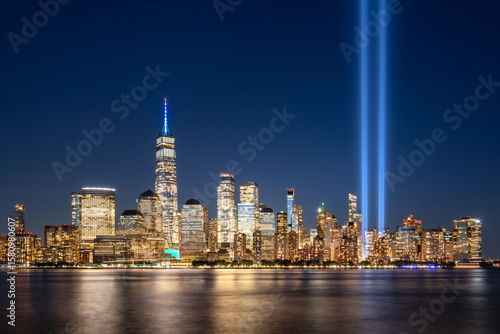 Photography Night view of Lower Manhattan skyline, illuminated skyscrapers and projection into sky of twin beams of light