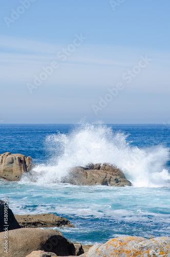 Dramatic ocean waves collide with rugged rocks on a sunny day, creating powerful splashes and a sense of natural energy at the coastline. Perfect for nature themes.