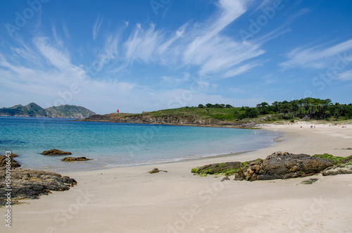 Tranquil sandy beach with turquoise sea, rocky coast, and lush greenery on a bright summer day. Ideal vacation destination and nature relaxation background.