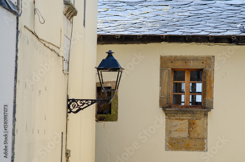 Charming close-up of an old stone window with wooden frame and classic black lantern on a rustic European house, evoking timeless village architecture.