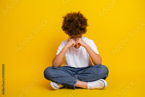 Fotografie Young boy in casual outfit sitting with thoughtful gesture on yellow background