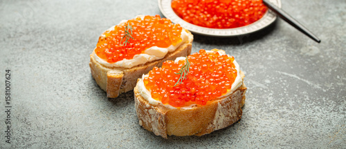 Fotografie Small metal plate with red salmon caviar and two caviar toasts canape on grey concrete background, festive luxury delicacy and appetizer