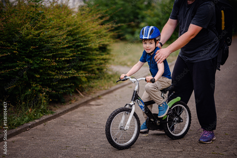 Obraz premium Parent Teaching Young Child to Ride Bike on Sidewalk