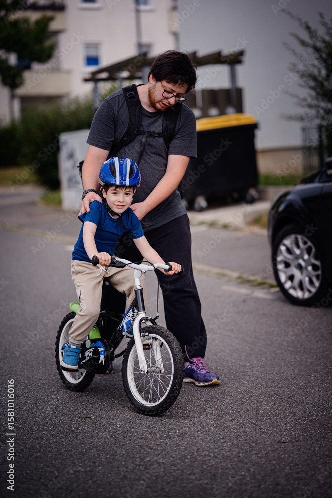 Obraz premium Parent Teaching Young Child to Ride Bike on Sidewalk