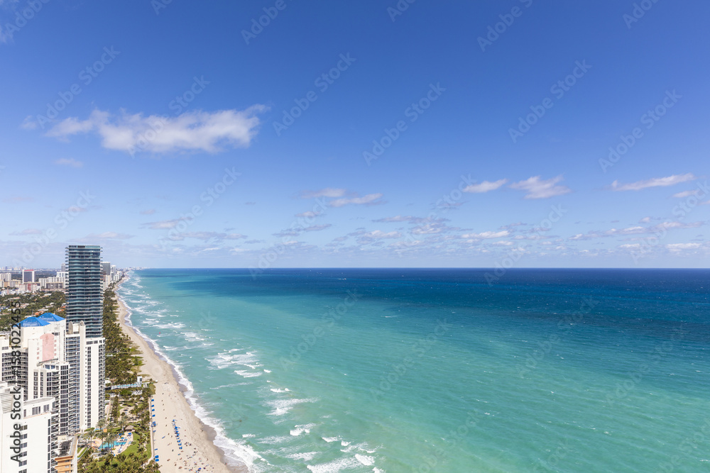 Aerial view of turquoise waters meeting the pristine white sands of the beach, juxtaposed against the towering buildings, Sunny Isles Beach, Florida, United States. Aerial view of turquoise waters meeting the pristine white sands of the beach, juxtaposed against the towering buildings, Sunny Isles Beach, Florida, United States.
