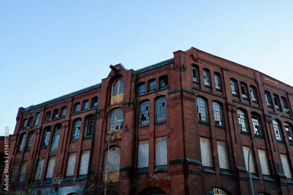 Obraz premium Altes Backsteingebäude mit zerbrochenen Fenstern und graffitierter Fassade bei blauem Himmel