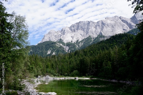 Grüner Bergsee vor felsigem Alpenmassiv unter wolkigem Sommerhimmel