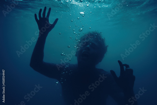 Terrified man drowning underwater reaching toward surface in state of panic and desperation with bubbles rising in dark blue sea
