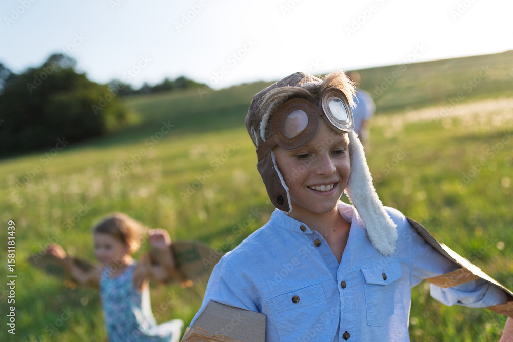 Naklejka premium Siblings dressed as pilots running through a sunny field.