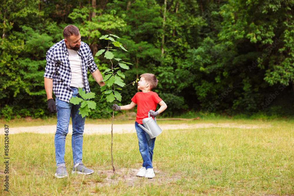 Fototapeta premium Father and his son planting tree into soil outdoors, space for text