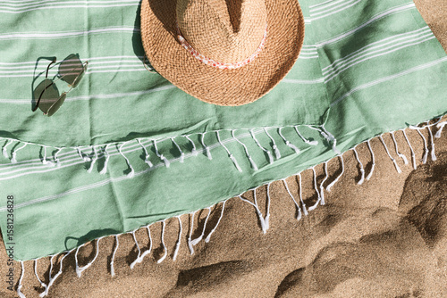 Fototapeta Naklejka Na Ścianę i Meble -  Green towel, straw hat, sunglasses on beach sand background. Aesthetic lifestyle, summer vacation concept. Sunbathing, beach party, holiday picnic. Travel fashionable blog, social media, top view.