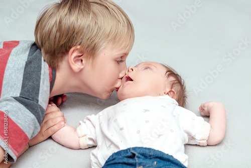 Big brother lovingly kissing his little newborn infant baby sister girl.older kid meeting new sibling,lay in bed together.Family with children at home.Love,tenderness