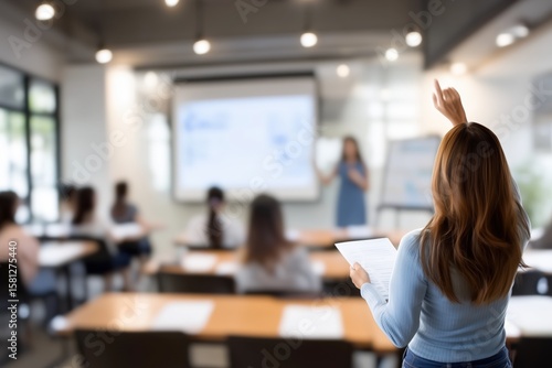 A student raises her hand in a modern classroom, indicating active participation during a presentation