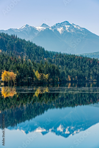 Autumn foliage and snowy mountains are reflecting in Gun Lake near Gold Bridge, British Columbia, Canada