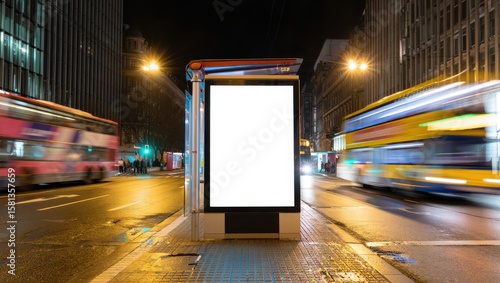 Blank advertising billboard at a busy city bus stop at night with blurred buses