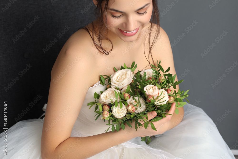 Naklejka premium Beautiful young bride in wedding dress with bouquet sitting on dark background, closeup