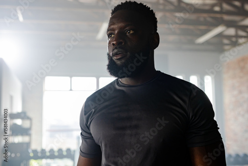 African American man wearing fitted black shirt pausing workout in studio with dumbbell rack