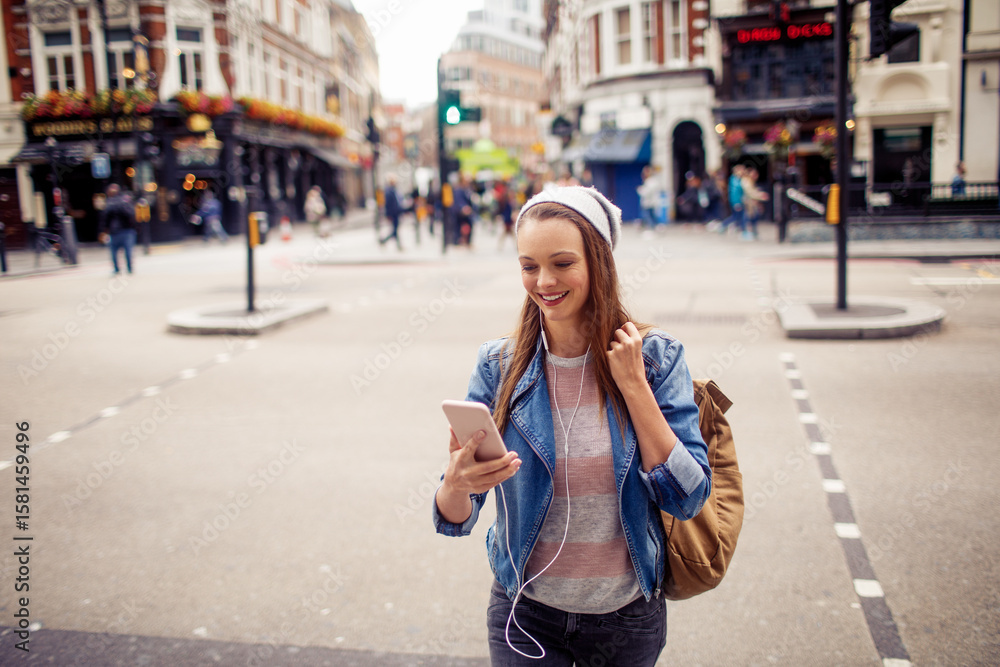 Fototapeta premium Young woman using a smart phone while crossing the street in london