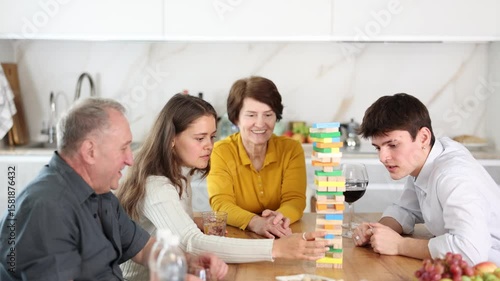 Smiling interested young girl having fun enjoying tower building game with husband and elderly parents-in-law during family weekend, showcasing intergenerational bonding