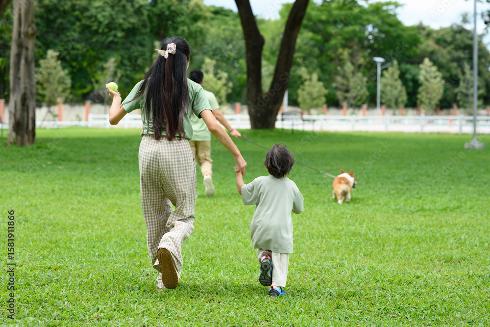 Rear view of a mother and child holding hands while running with their dog on a sunny day in the park Rear view of a mother and child holding hands while running with their dog on a sunny day in the park