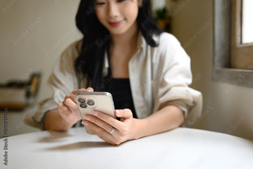 Fototapeta premium Close up of a woman hands holding and using a smartphone while seated at a cafe table