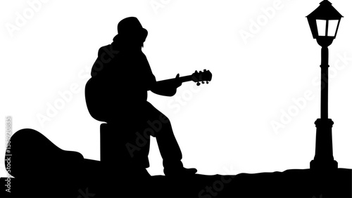 Silhouette of a musician with guitar sitting by a lamp post on a street corner performing music