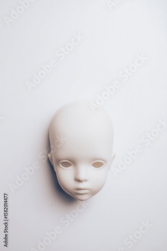 A blank, featureless doll head rests on a white background. The head is smooth and unpainted, lacking any distinct facial features or expressions.