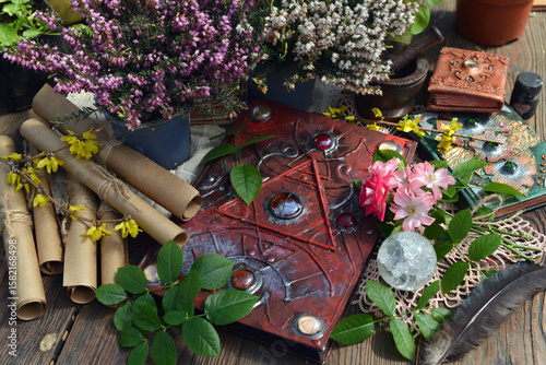 Mystic still life with decorated magic book of spells, veres flowers, manuscripts, crystal, herbs and witchy ritual objects on old table. Occult, esoteric and wicca concept