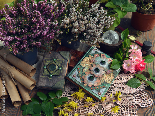 Mystic still life with decorated magic book of spells, veres flowers, manuscripts, crystal, herbs and witchy ritual objects on old table. Occult, esoteric and wicca concept