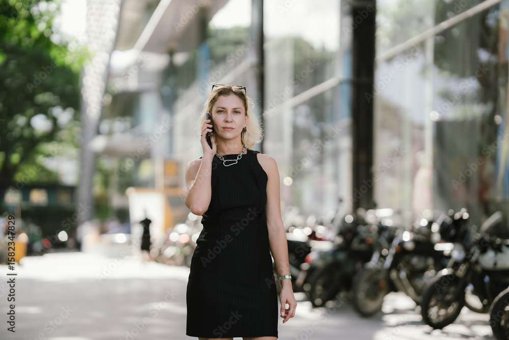 Fototapeta premium A confident businesswoman in a black dress and sunglasses walks through the city streets, exuding elegance, style, and empowerment in a modern, professional urban lifestyle