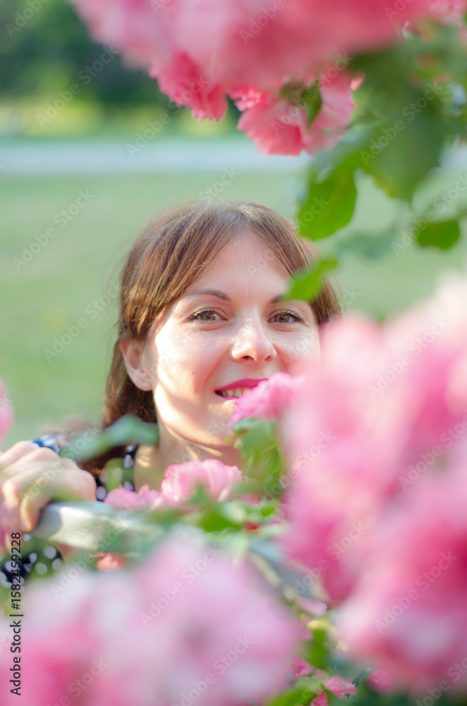 Fototapeta premium Beautiful young woman in a polka dot dress with roses, in a park on a sunny day