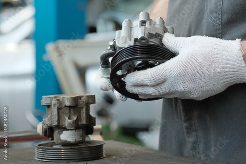 Garage. Car service.An auto mechanic prepares a new car power steering pump for replacement. There is a faulty power steering pump nearby on the desktop.