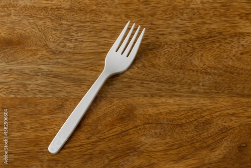 Disposable white plastic fork placed on a wooden table © The 2R Artificiality