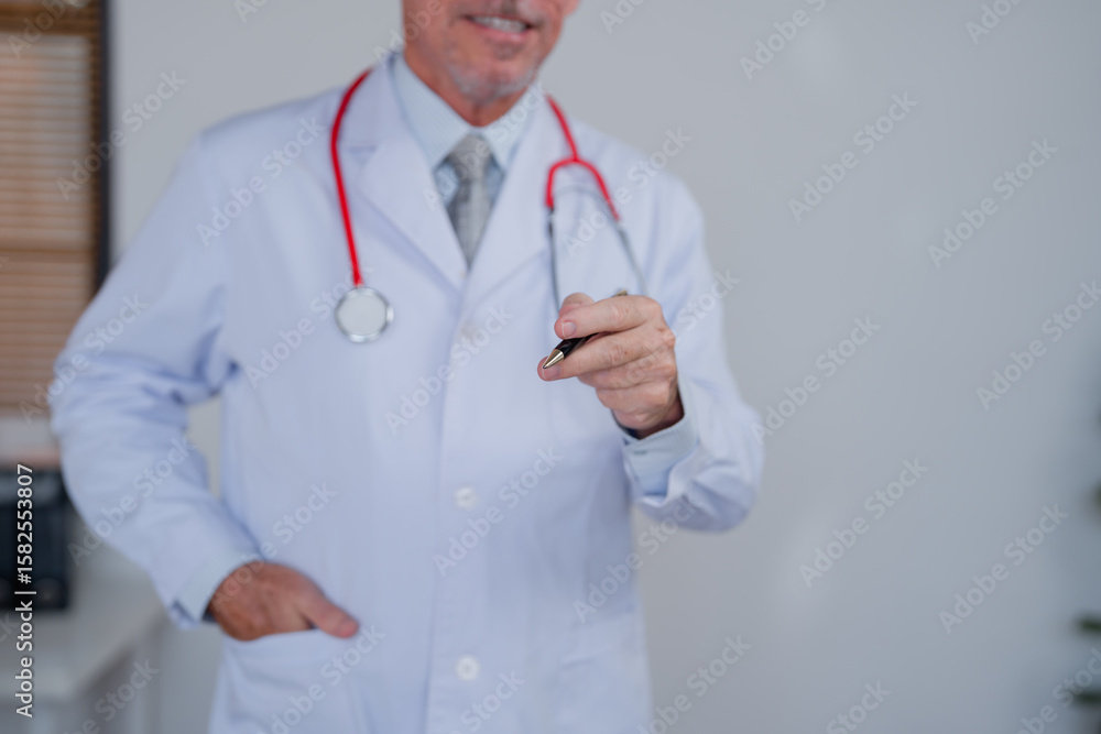 Senior male doctor wearing lab coat and stethoscope is holding a pen and smiling, suggesting a positive healthcare experience in a medical office Senior male doctor wearing lab coat and stethoscope is holding a pen and smiling, suggesting a positive healthcare experience in a medical office