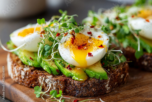Cropped close-up of open-faced rye sandwich with avocado slices, soft-boiled egg, chili flakes, and microgreens