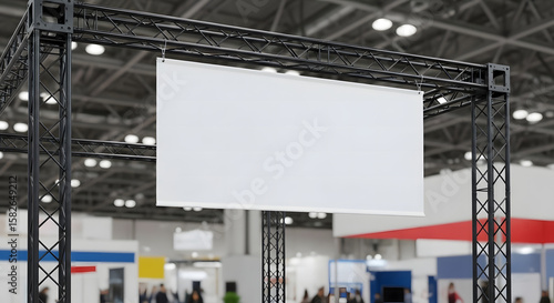 Blank white banner hanging from black metal truss structure in a blurry exhibition hall, ready for custom text or logo, a professional mock-up photo.