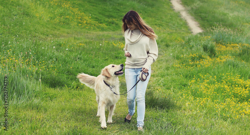 Owner woman walking with Golden Retriever dog on leash in summer park