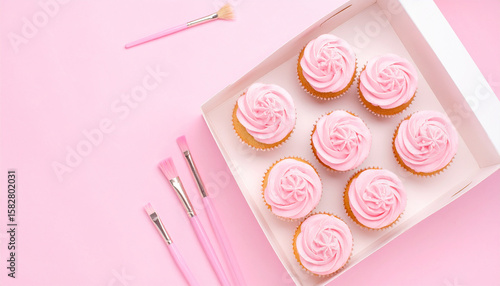 Pink Cupcakes and Makeup Brushes: A delightful flat lay showcasing eight delicious pink cupcakes arranged in a box alongside a set of pink makeup brushes, all set against a vibrant pink background.