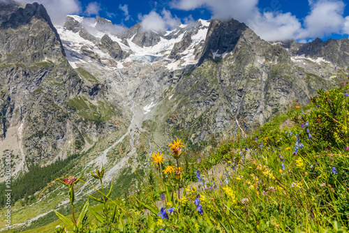 Courmayeur mountain valleys Val Veny and Val Ferret in the Alps in Italy. Rocky snow mountain peaks above green blooming flower valley on sunny day. Tour du Montblanc mountain landscape in the Alps