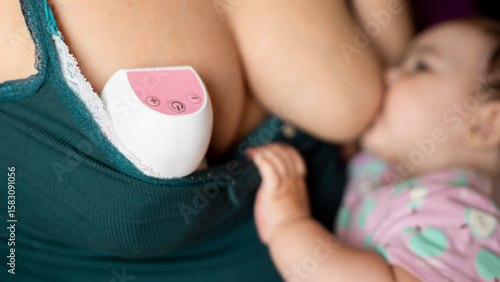 Mother breastfeeding newborn baby with electric breast pump on chest for milk supply and pumping at home