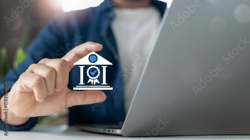Photography Hand holding certified institution icon with check mark in front of laptop, symbolizing trust, approval, financial institution, or government certification