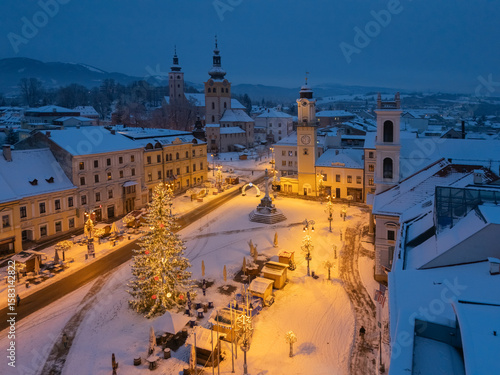 Aerial view of a snow-covered square, adorned with a Christmas tree and illuminated by warm lights, contrasting against the dusk, BanskÃ¡ Bystrica, BanskobystrickÃ½ kraj, Slovakia.