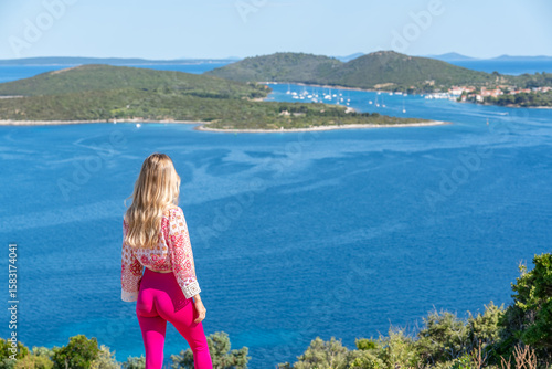 Blonde woman stands on a scenic overlook admiring the deep blue coastline of Croatian islands. A visual metaphor for personal growth and exploration