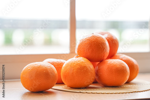A close-up shot showing a pile of fresh, ripe oranges near a window.