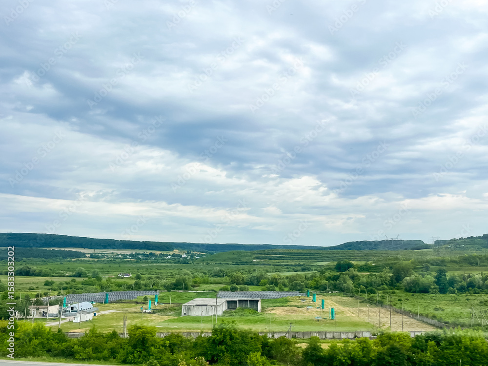 Naklejka premium Expansive rural landscape with cloudy sky and lush greenery.