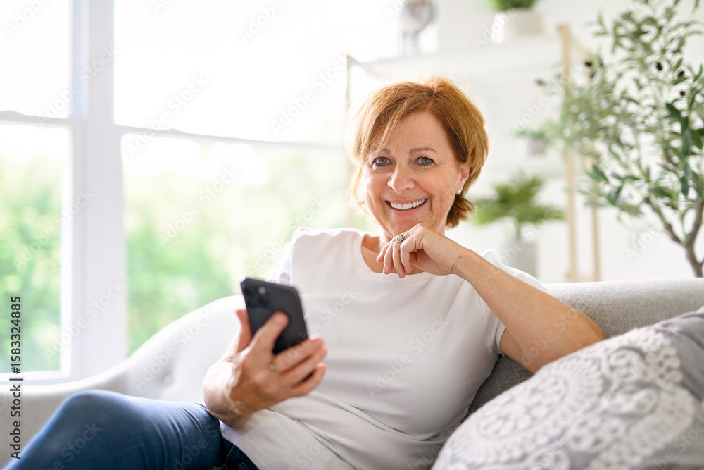 senior woman relaxing at home on the sofa reading her text messages on her mobile phone with a quiet smile senior woman relaxing at home on the sofa reading her text messages on her mobile phone with a quiet smile