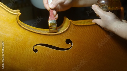 Obraz na plátně Skilled luthier varnishing wooden cello soundboard with traditional brush, highl
