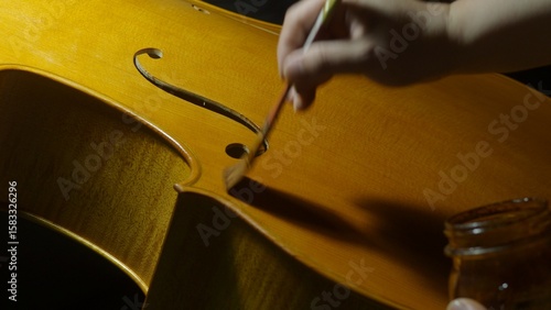 Fotografie Skilled luthier carefully brushing varnish onto cello soundboard, highlighting c